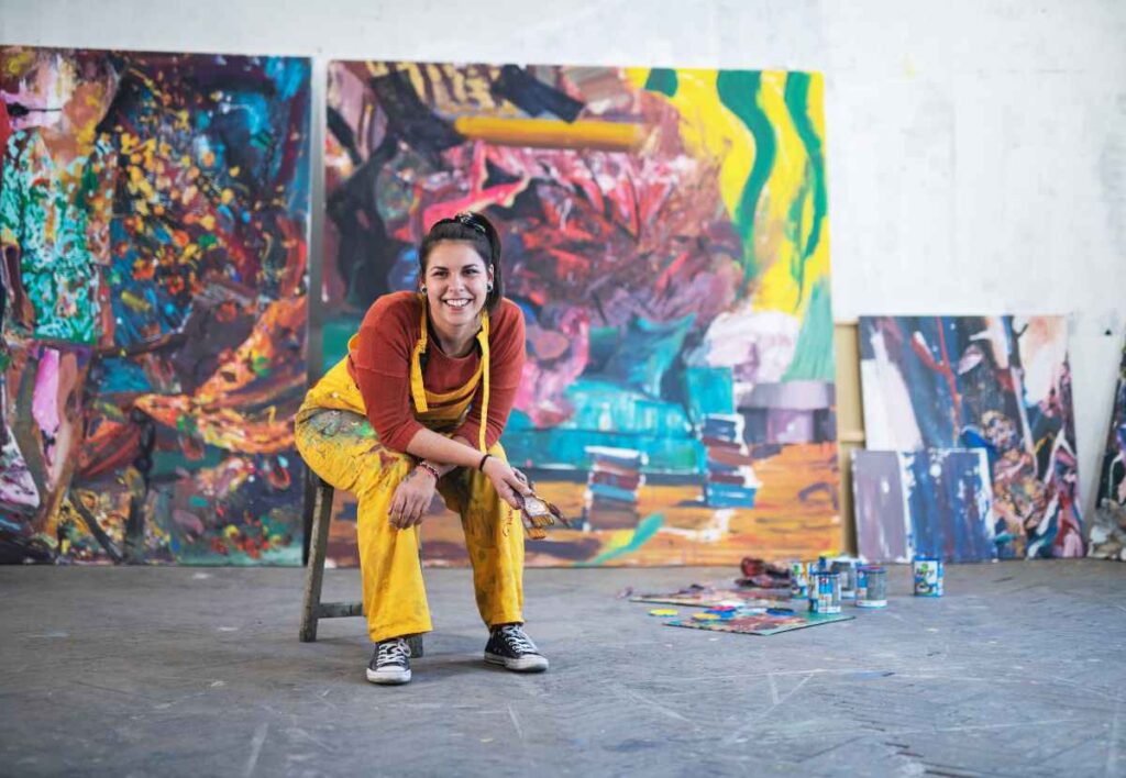 artist in posing in front of her mural painting on a building